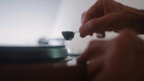 Eine Hand bedient den Plattenspieler, setzt die Nadel auf die Platte