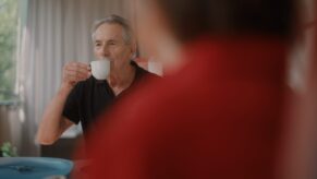 Älterer Mann am Balkon trinkt aus Kaffeetasse