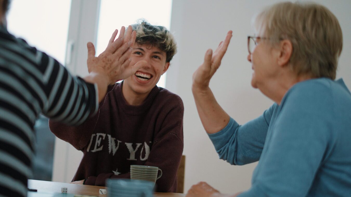 Ein junger Mann, lacht und gibt zwei älteren Damen ein High-Five