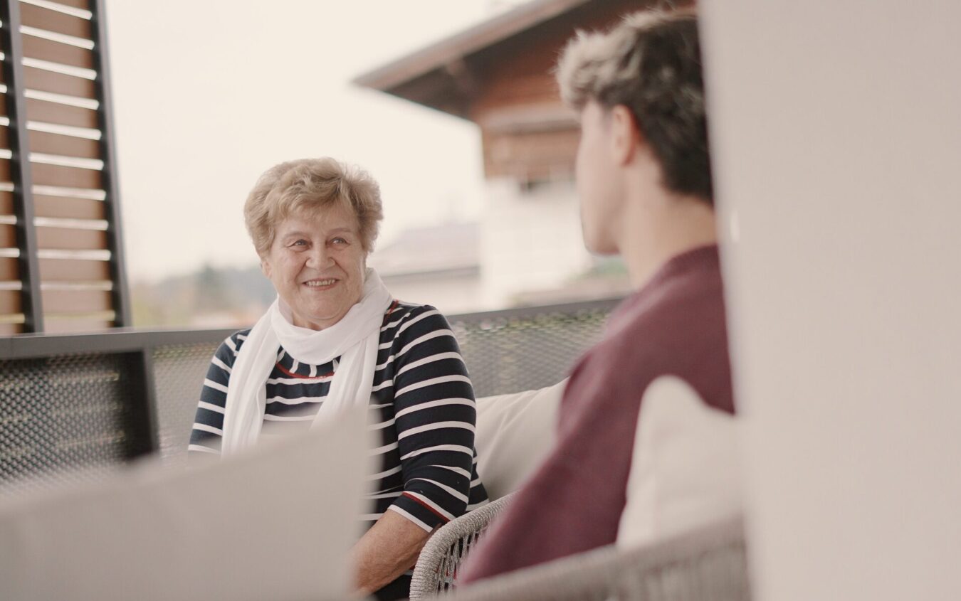 Ältere Frau sitzt mit jungem Mann auf Balkon