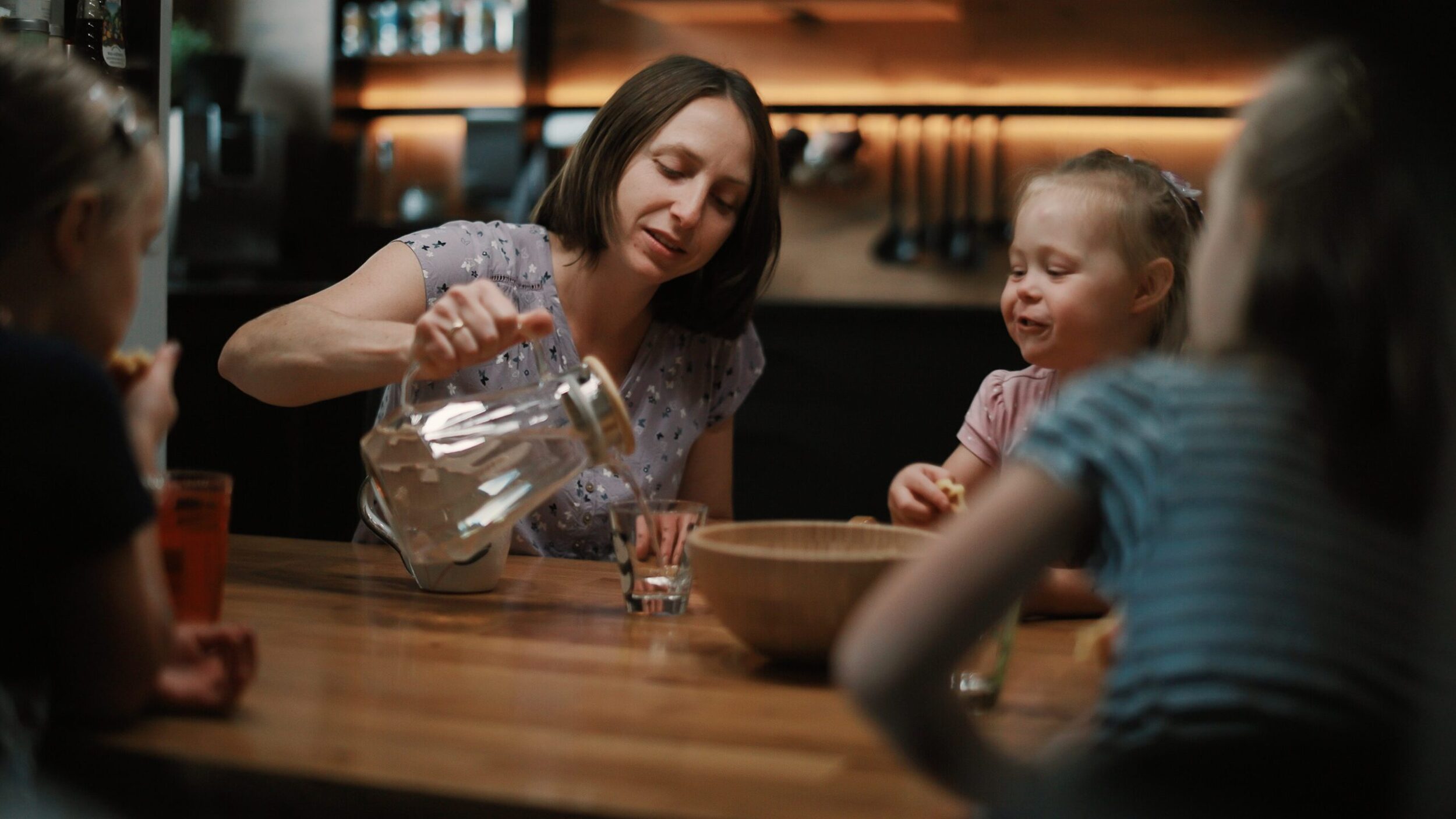 Am Essenstisch, Mutter schenkt Wasser in ein Glas, kleines Mädchen schaut zu