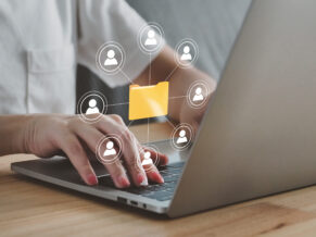 Am Laptop, Hände tippen am Laptop, virtueller Verteiler im Vordergrund