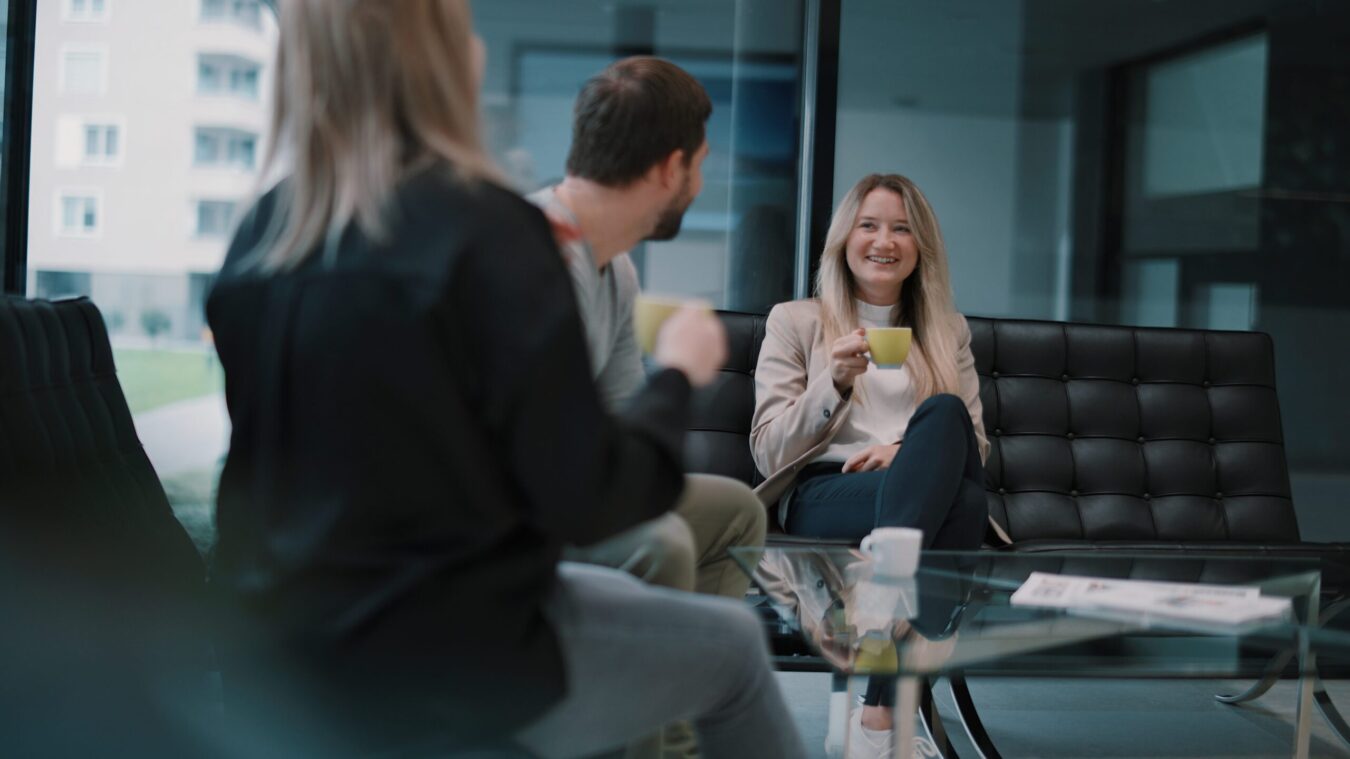 Besprechungssitutation, eine Mann schaut auf eine junge Dame mit langen blonden Haaren, die eine Tasse in der Hand kält