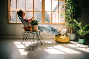Frau gemütlich im Korbstuhl vor Fenster
